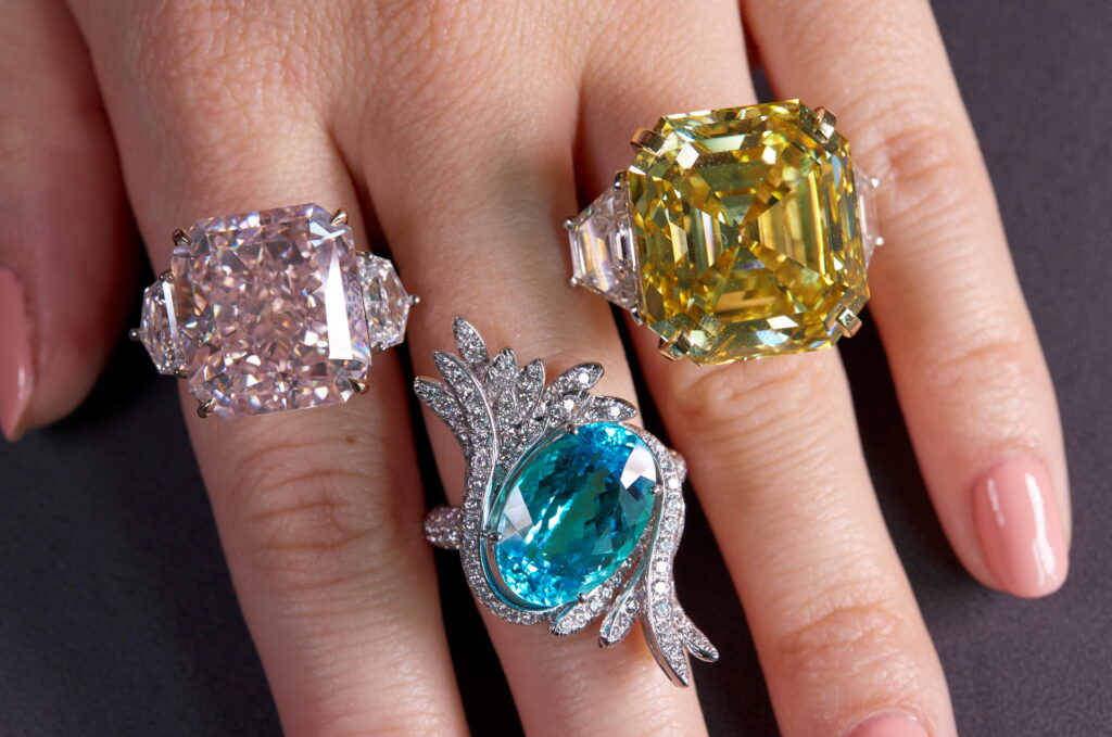 A staff member wears an orange-pink diamond ring, a tourmaline and diamond ring and a yellow diamond ring during a preview at Sotheby's, before their auction sale in Geneva
